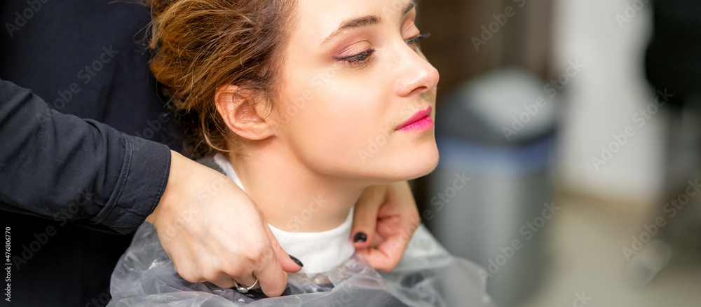 A hairdresser is covering a female neck with a cape for a female client in a beauty salon, close up