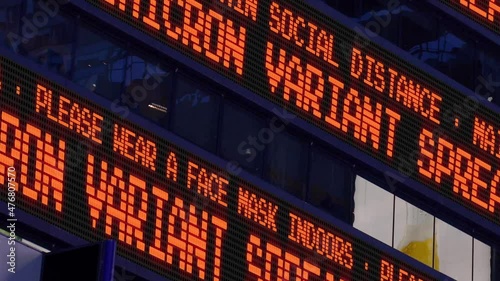 A fictional stock market ticker informs pedestrians about the Omicron Variant strain. Masks and social distancing were common practices to slow down the spread of COVID during the pandemic of 2021.