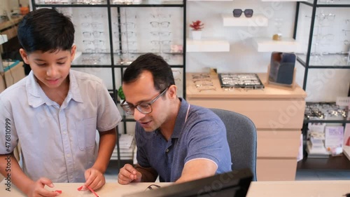 Indian father sit and discuss with his son to select eyeglasses or sunglasses in optical shop with happiness.