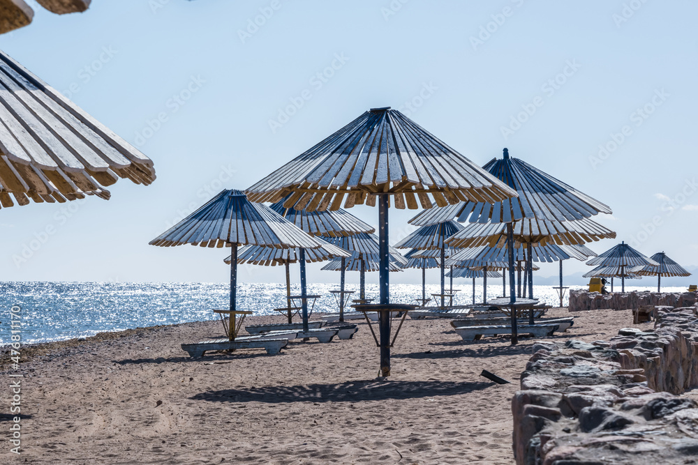 wooden beach umbrellas and sun loungers by the red sea in bright sunny day