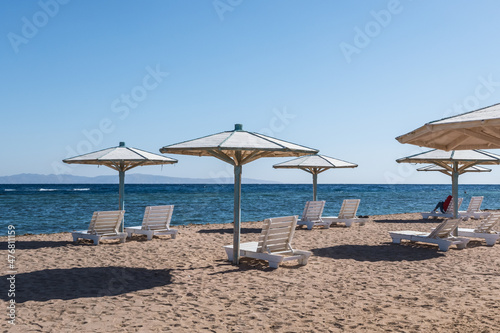 wooden beach umbrellas and sun loungers by the red sea in bright sunny day