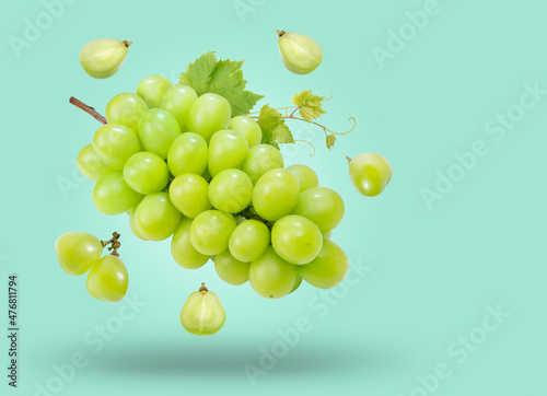 Sweet Green grape with leaves falling in the air isolated on green background, Shine Muscat Grape on green background With clipping path.