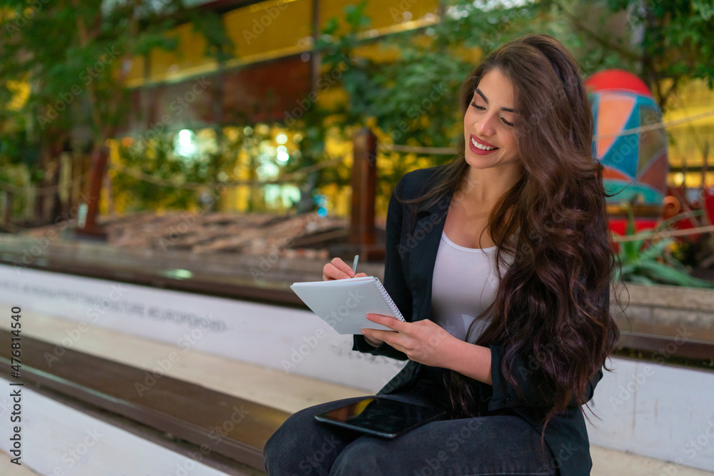 Obraz premium Young attractive business woman using a digital tablet and writing in her notebook