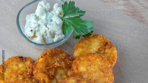 Close-up view of fried potato pancakes with cream sauce and leaf of parsley.
