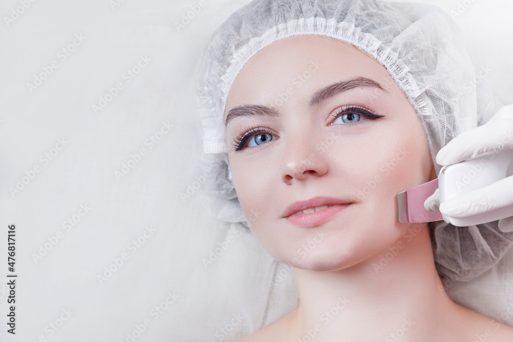 Cosmetologist,beautician in white gloves making facial treatment with ultrasonic spatula to young woman,face skin scrubber treatment with ultrasonic spatula,facial cleansing procedure Cosmetologist,beautician in white gloves making facial treatment with ultrasonic spatula to young woman,face skin scrubber treatment with ultrasonic spatula,facial cleansing procedure