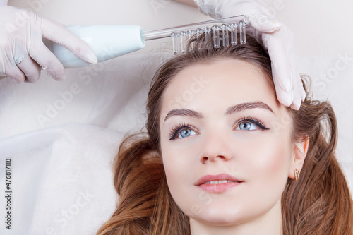 The doctor-cosmetologist makes the procedure Microcurrent therapy On the hair of a beautiful, young woman in a beauty salon.Cosmetology and professional skin care. photo