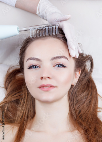 The doctor-cosmetologist makes the procedure Microcurrent therapy On the hair of a beautiful, young woman in a beauty salon.Cosmetology and professional skin care. photo
