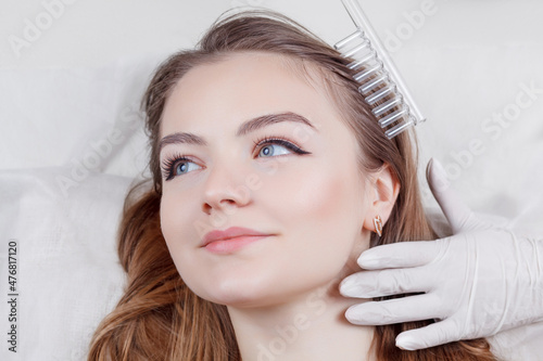 The doctor-cosmetologist makes the procedure Microcurrent therapy On the hair of a beautiful, young woman in a beauty salon.Cosmetology and professional skin care.
