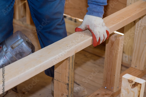 Builder inside wooden houseman in nailing wooden beams works for construction using an air hammer