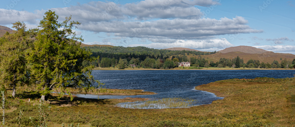 A panoramic landscape view of a large house in the distance on the other side of the lake