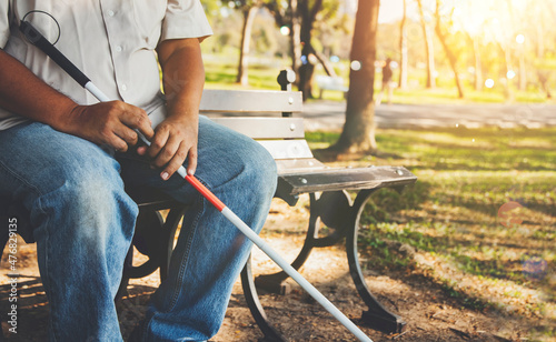 Elderly blind man with a blind cane sits alone on a park bench : Lind man who wants peace and lives in solitude concept.