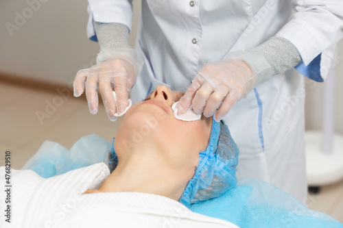 Photo of professional female cosmetologist using sponges to wash the face of a woman client preparing for a cosmetic procedure. Rejuvenating and moisturizing procedures