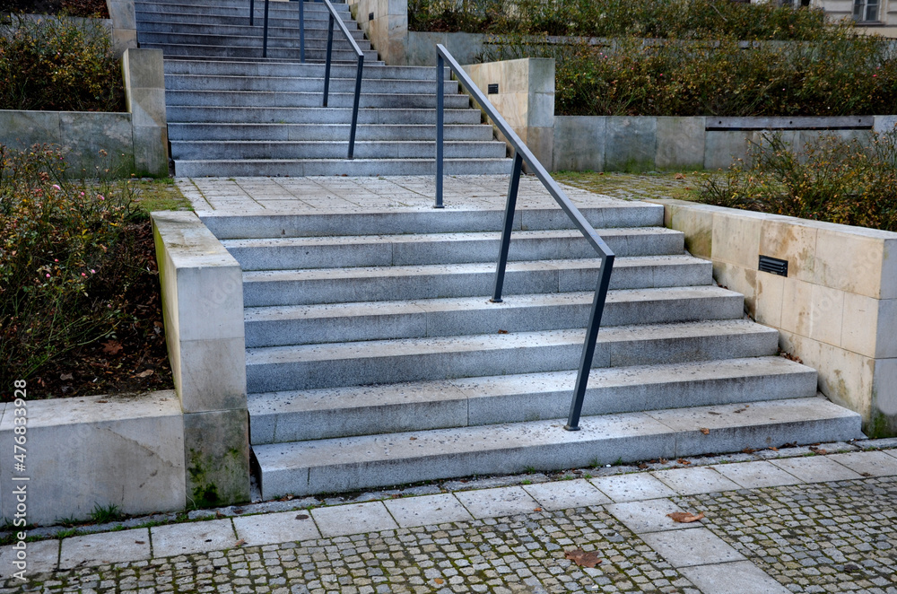 staircase with a centrally located railing. The railing goes in the middle of the stairs. metal park handle. in the park on the square. stone element, square tiles