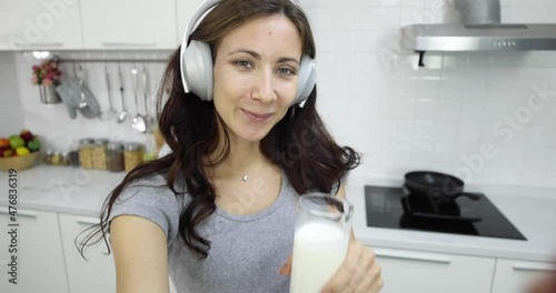 Positive pregnant female shooting selfie video and drinking refreshing milk while looking at camera and dancing in kitchen at home