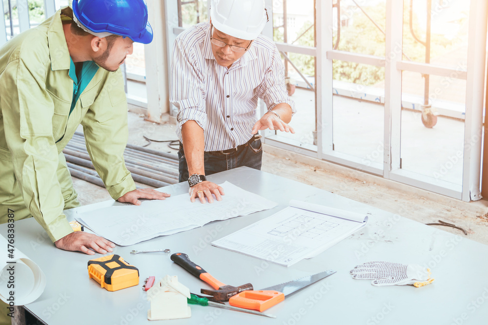Engineer and worker looking home plans with helmet, craftsman tool and home model on workplace at construction site. Engineer and worker looking home plans with helmet, craftsman tool and home model on workplace at construction site.
