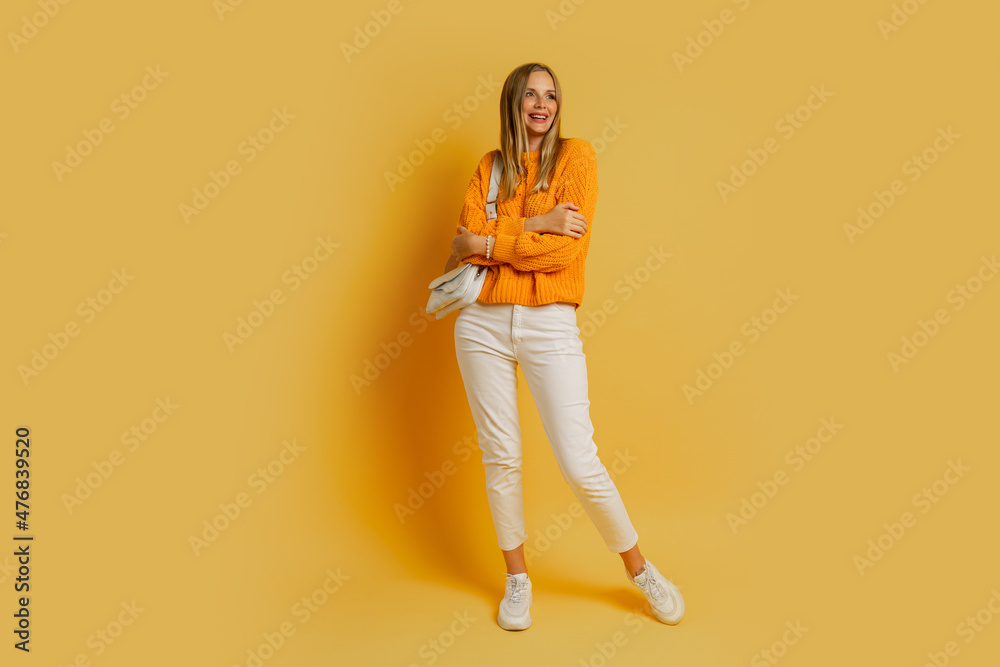Pretty   blond  woman  in   trendy autumn outfit   posing on yellow background in studio.  Holding  white leather bag.  Full lenght.