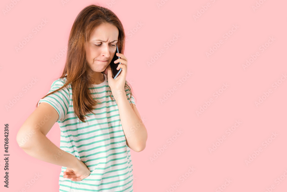 A distressed beautiful brunette girl is talking on the phone. Portrait of a woman on a pink background who learns bad news on the phone. A distressed beautiful brunette girl is talking on the phone. Portrait of a woman on a pink background who learns bad news on the phone.