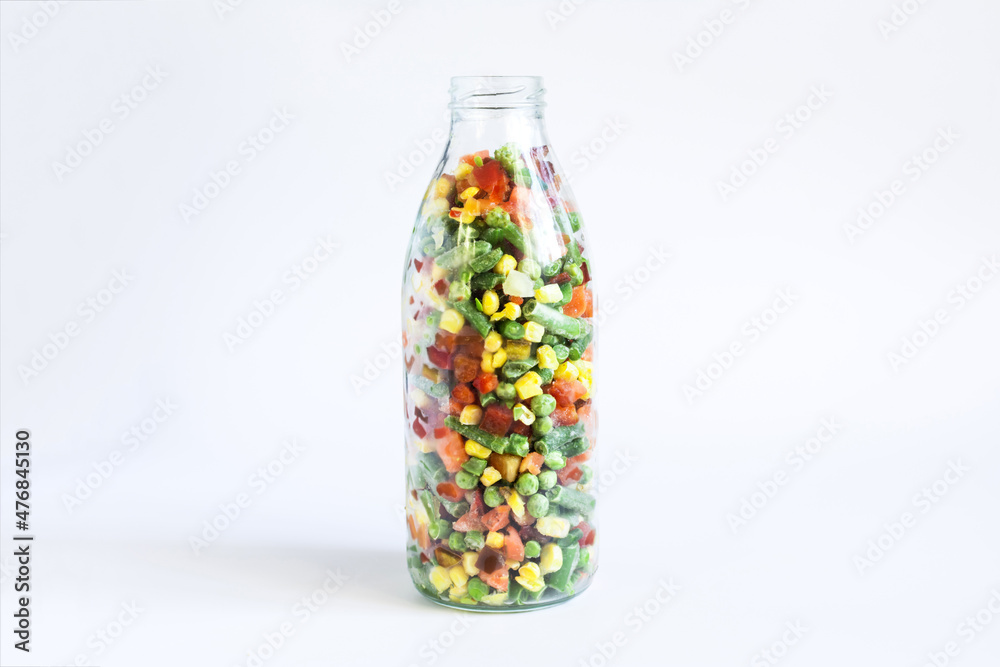 The concept of using quick-frozen products, a transparent bottle with a mixture of frozen vegetables on a light background The concept of using quick-frozen products, a transparent bottle with a mixture of frozen vegetables on a light background