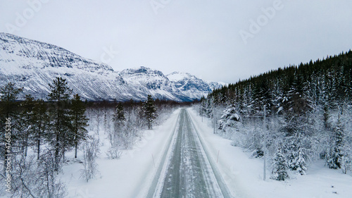 Snowy Road surrounded by a forest and mountains in Norway - Drone Perspective Landscape Photography