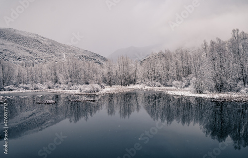 Peisaje nevado un bonito lago con arboles y montañas de fondo © Marian