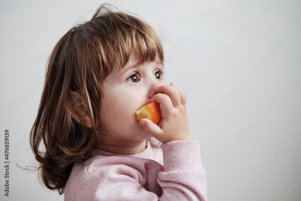 Adorable baby girl eating a slice of orange isolated on white background. Adorable baby girl eating a slice of orange isolated on white background.