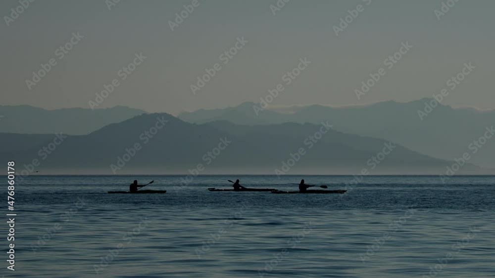 Silhouettes of tourists on kayaks moving on mountain range background. Summer recreation on Kamchatka peninsula, Russia. Silhouettes of tourists on kayaks moving on mountain range background. Summer recreation on Kamchatka peninsula, Russia.