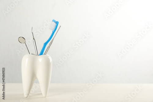 Tooth shaped holder with set of dentist's tools and brush on wooden table. Space for text
