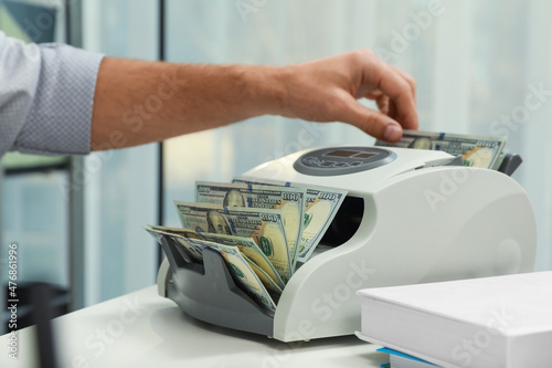 Fotografi Man using banknote counter at white table indoors, closeup