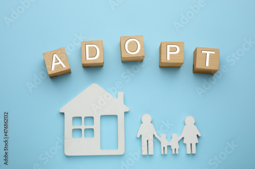 Family figure, house and word Adopt made of cubes on light blue background, flat lay