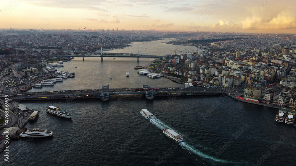 Aerial view of Galata bridge, bottom, and Halic metro bridge located in the Golden horn waterway, city of Istanbul, Turkey, during sunset.