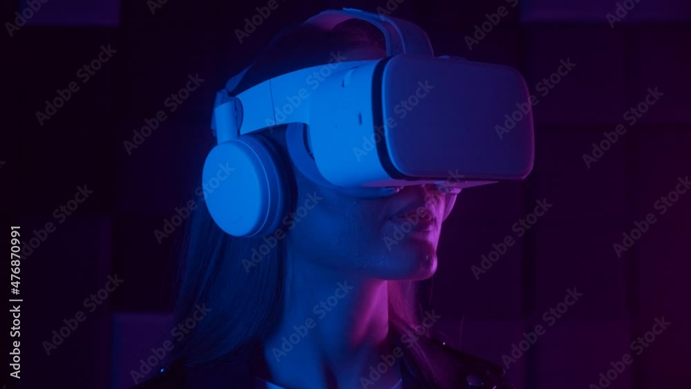 Young woman in futuristic VR headset interacting with cyberspace under neon light in dark studio. Augmented reality, science, future technology concept Young woman in futuristic VR headset interacting with cyberspace under neon light in dark studio. Augmented reality, science, future technology concept
