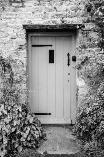 Wooden door entrance into rural cottage house in Bibury, Cotswolds, Egland, UK. Vintage wooden door on stone wall with green bushes photo