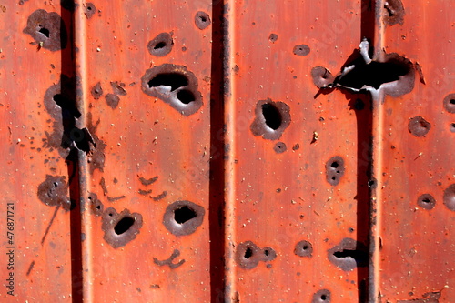 Side of shipping container rusted metal plate heavily damaged by shrapnel during war covered with faded dilapidated paint texture background wallpaper photo