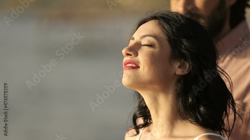 Girl with closed eyes stands near the coast, a brutal man approaches him and hugs her from behind