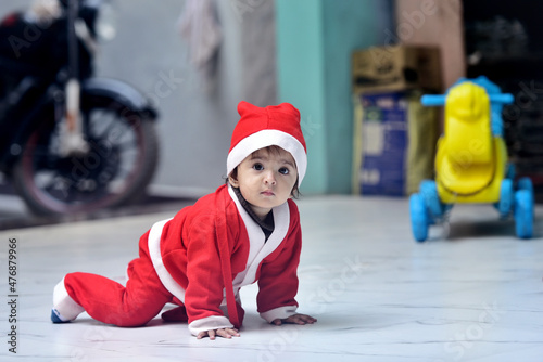 13 months old Indian baby girl wearing Santa Claus on Christmas Day sitting on the floor and looking at the camera