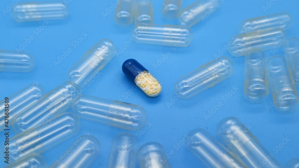 A medicine capsule in the middle of empty capsules. Close-up, blue background, rotation. A medicine capsule in the middle of empty capsules. Close-up, blue background, rotation.