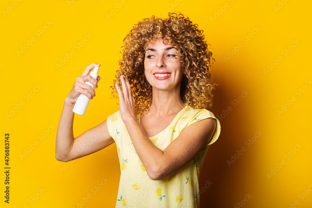 smiling young woman sprays with spray on yellow background. Hair Styling
