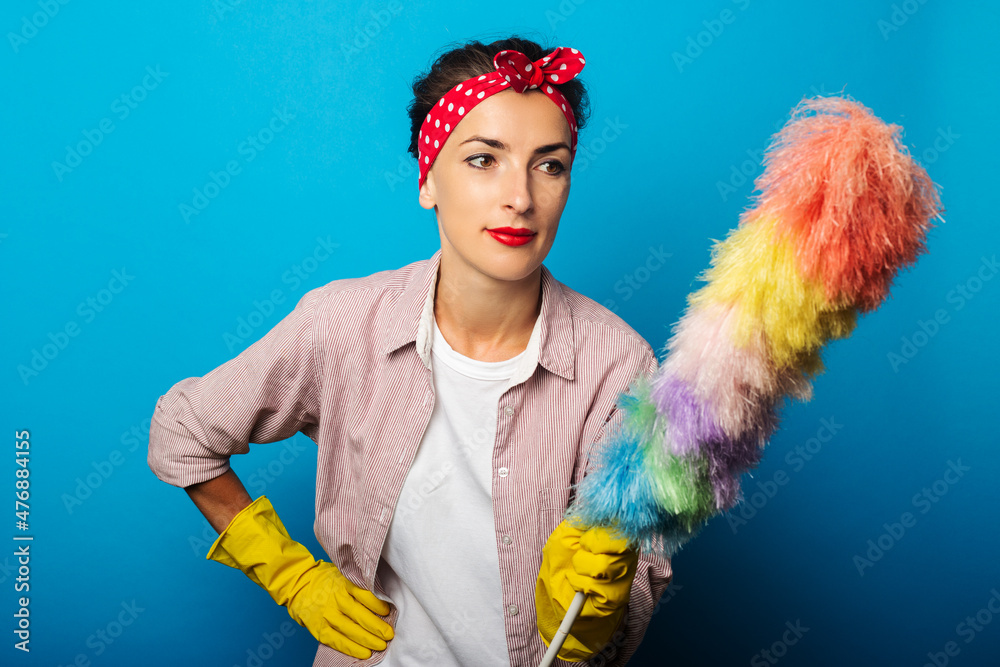 Smiling young woman in gloves holding dust brush on blue background. Smiling young woman in gloves holding dust brush on blue background.