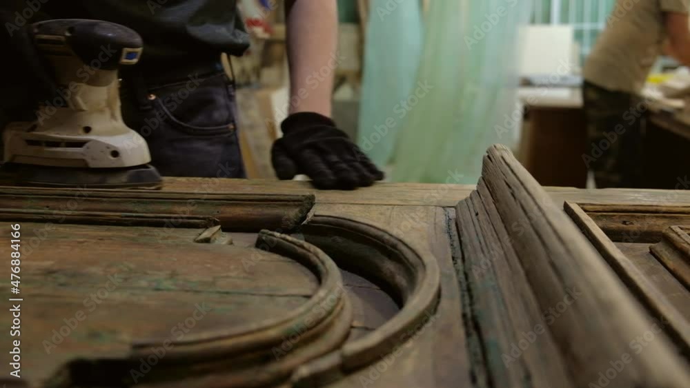 Carpenter sands wooden door with sanding machine. Restoration of vintage door. Removing paint