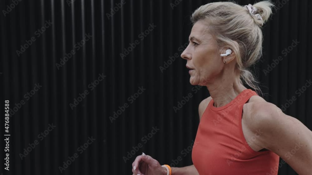 Aged sporty woman jogging outdoors in earphones