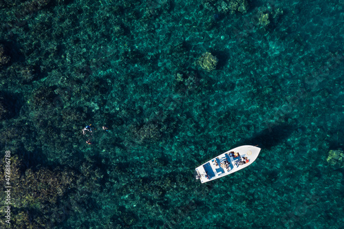 Aerial view of boat and snorkeling activity with clear water showing rocks and corals. © Djuneid