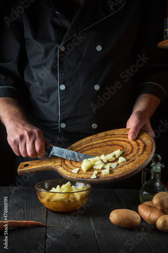 The chef prepares raw potatoes for lunch or dinner. Close-up of a cook hands while working in a restaurant kitchen
