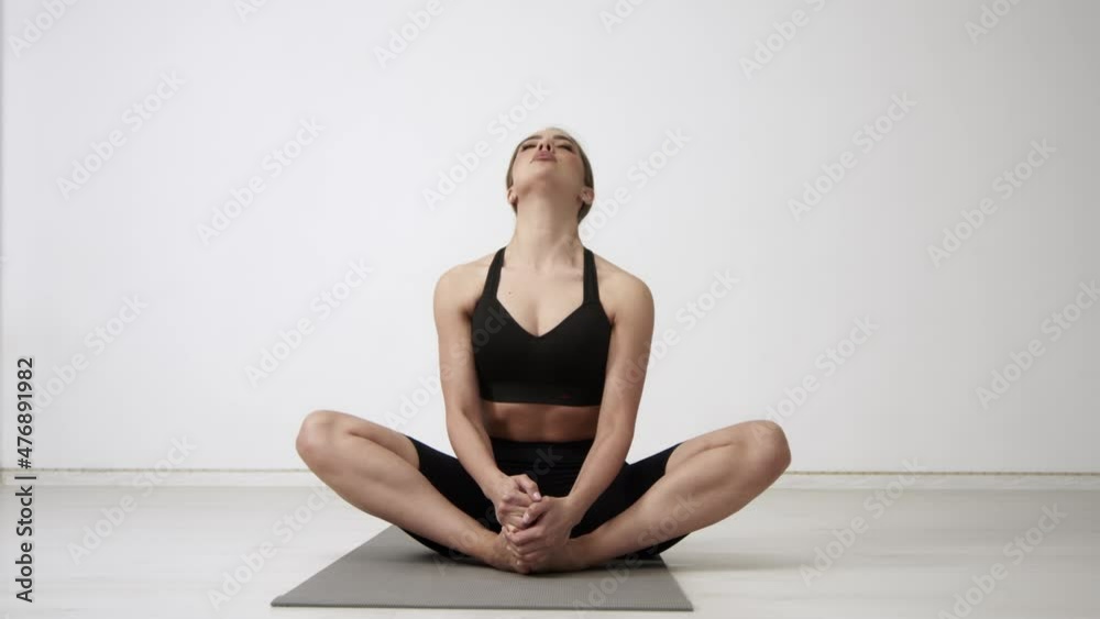 Young brunette woman practicing yoga and stretching exercise in white studio, attractive girl in black sportswear seated cross-legged lotus pose work out on gym mat Young brunette woman practicing yoga and stretching exercise in white studio, attractive girl in black sportswear seated cross-legged lotus pose work out on gym mat