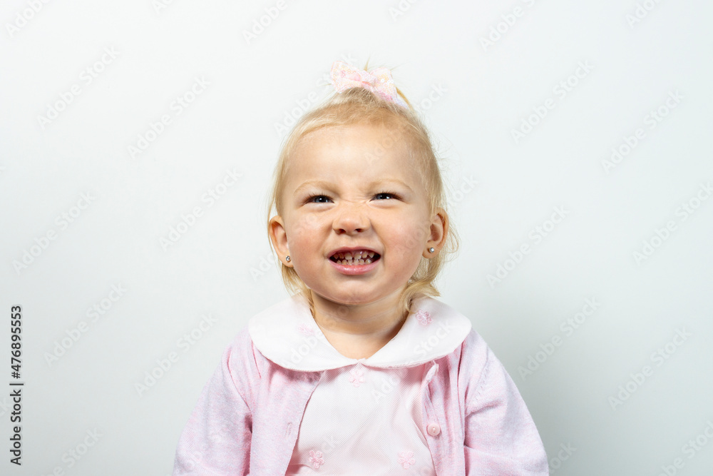 Little kid girl in dress grimaces on a light background Little kid girl in dress grimaces on a light background