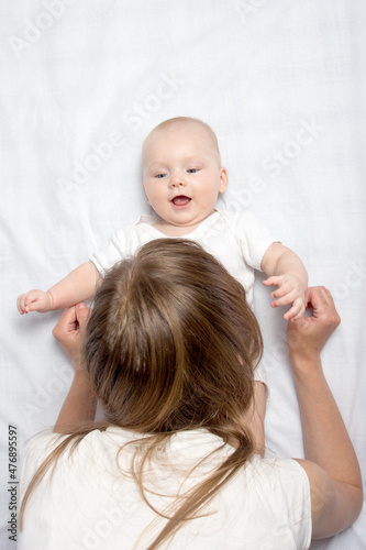 Mom plays with a little baby on the bed with a white sheet. Flat lay, top view