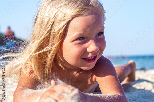 Cheerful child girl is played lying on the sandy beach on a sunny day. © Alex