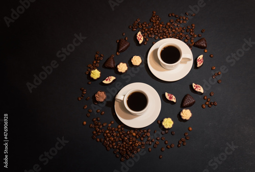 Cups of coffee, coffee beans and chocolate candies on dark background.