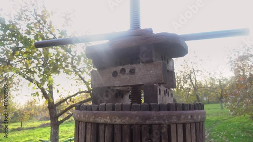 An old wooden press for making freshly squeezed juice against the background of sunlight. Squeezing of fresh apples in wooden press to bucket to produce cider in village. Food processing 4k