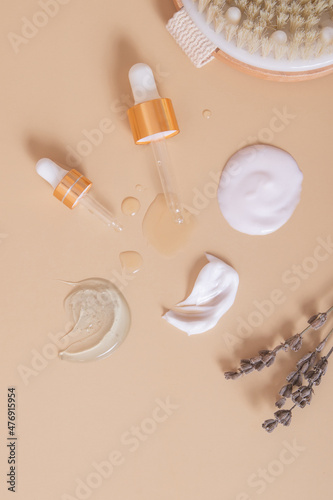 Smears of various cosmetic products and pipettes on a beige background with dry lavender and a body brush.