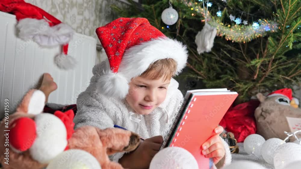 Adorable boy Christmas child in red hat writing letter about wishes to Santa Claus and, Xmas gift wish list, Christmas or New Year cozy holidays concept Adorable boy Christmas child in red hat writing letter about wishes to Santa Claus and, Xmas gift wish list, Christmas or New Year cozy holidays concept